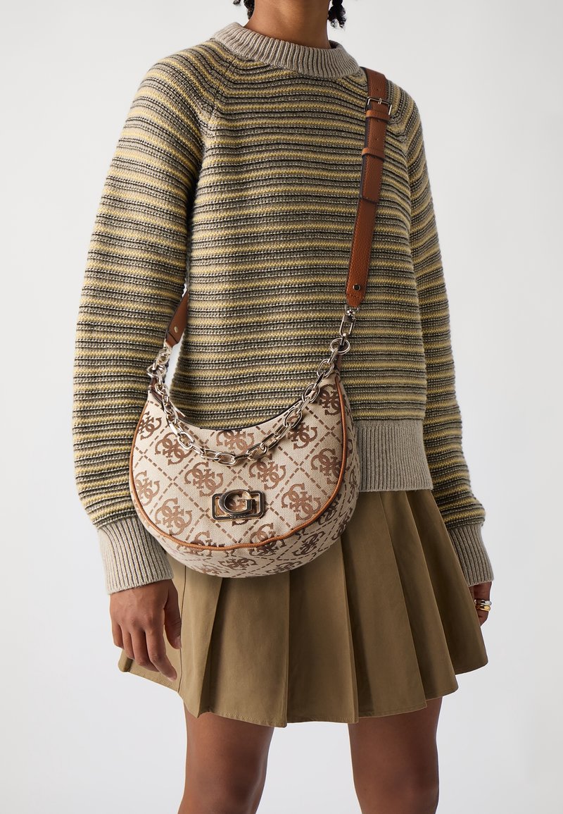 Personne portant un pull en maille rayé et une jupe plissée, portant un sac à épaule beige et marron à motif avec un détail chaîne.