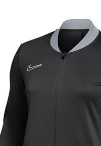 Zwarte sportjack met grijze kraag, rits aan de voorkant en klein wit Nike-logo aan de linkerkant. Gladde textuur en aansluitende pasvorm.
