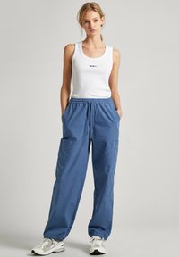 Pantaloni jogger leggeri in cotone blu con polsini elasticizzati, dotati di tasche laterali e vita regolabile con coulisse, abbinati a una canotta bianca aderente.