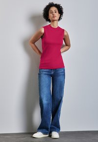 Läpinäkyvä ilman hihoja oleva paita kirkkaan vaaleanpunaisena, yhdistettynä väljiksi leikattuihin sinisiin farkkuihin ja valkoisiin tennareihin. Sileä kangas ja pyöreä kaula-aukko.