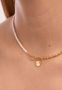 Collana in perle di resina e oro con piccole perle bianche a forma di riso e perle cilindriche in oro, impreziosita da un ciondolo rotondo che riporta la parola "BINGULAR."