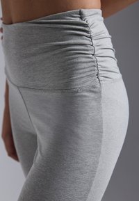 High-waisted grey leggings featuring gathered texture at the waistband, smooth fabric, and a fitted shape extending to mid-calf.