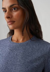 Grijs geribd gebreid T-shirt met een ronde hals, voorzien van een zachte textuur en een aansluitend ontwerp. Close-up van de schouder- en nekregio.