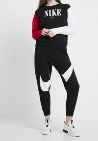 Black Nike sweatshirt with red, white sleeves and large logo; paired with black sweatpants featuring white accent shapes and cuffs.