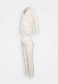 Zwangere pyjama-set in lichtbeige met zebraprint. Inclusief een bovenstuk met lange mouwen en een zak, en een lange broek. Zacht, rekbaar materiaal.
