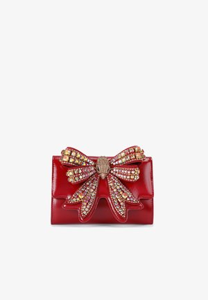 Borsa a tracolla in pelle rossa con un grande fiocco ornato di strass colorati e un dettaglio metallico centrale. Texture liscia, forma rettangolare.