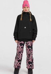 Felpa nera con cappuccio, tasca frontale, polsini a coste e un piccolo logo. Abbinata a pantaloni da neve rosa e grigi con motivo a fantasia, completati da stivali neri.