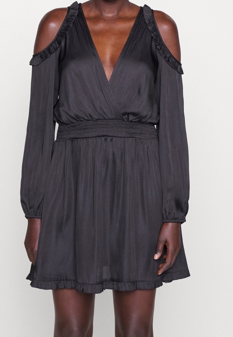 Svart klänning med djup V-ringning, kall axeldesign, långa ärmar, volangdetaljer vid axlarna och nederkant, samt en smockad midja. Slät textur.