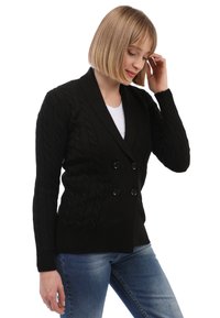 Schwarze Kabelstrick-Cardigan mit doppelt geknöpftem Vorderteil, ausgestattet mit zwei großen schwarzen Knöpfen und langen Ärmeln. Getragen über einem weißen Oberteil und blauen Jeans.