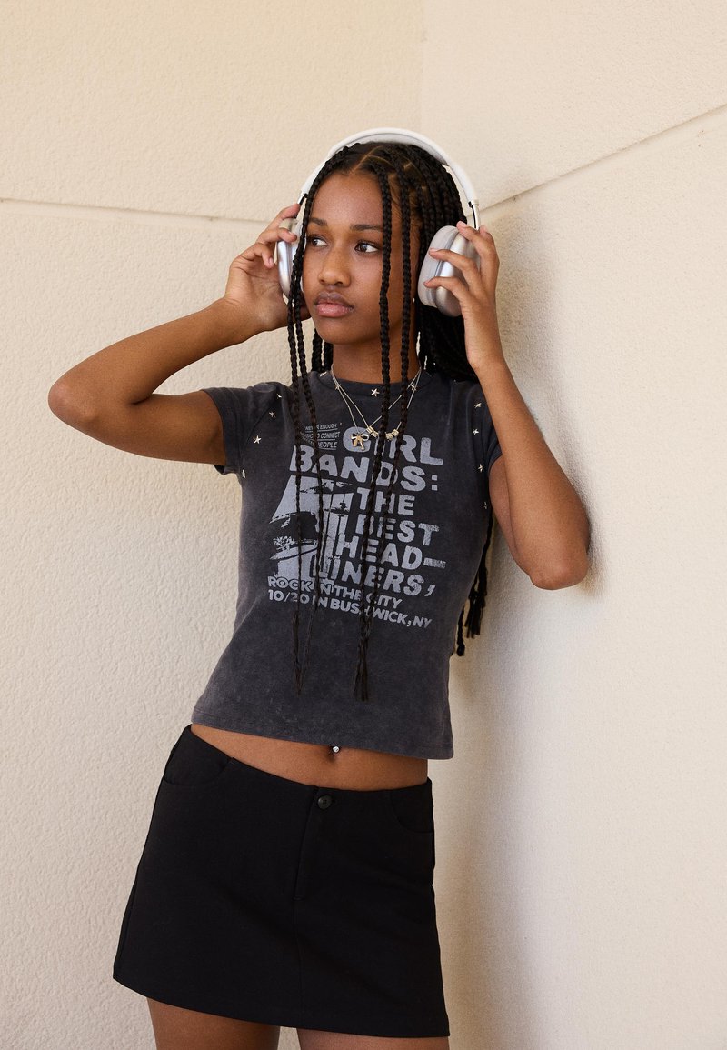 Black graphic t-shirt with white print and short sleeves, paired with a black mini skirt. Wearing silver headphones and layered necklaces.