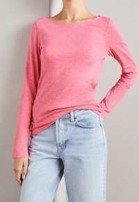 Langärmliges rosa T-Shirt mit U-Boot-Ausschnitt, aus einem strukturierten Stoff, kombiniert mit hellblauen, hoch taillierten Jeans.