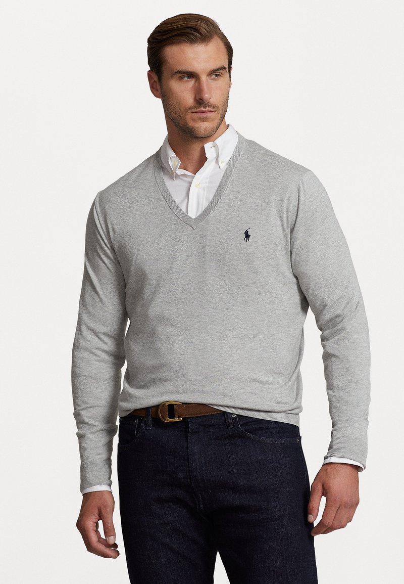 Gray v-neck sweater made of soft knit fabric. Features a small blue logo on the left chest, paired with a white collared shirt and dark jeans.