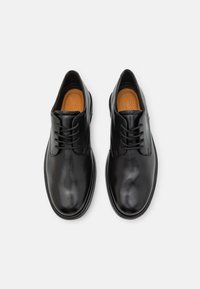 Scarpe in pelle nera con punte arrotondate, chiusura con lacci, finitura liscia e solette in contrasto color tan. Design minimalista, senza motivi visibili.