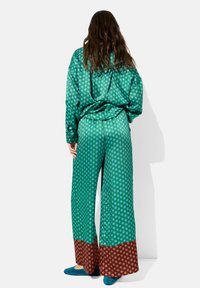 Zielony satynowy zestaw w kropki, składający się z luźnej bluzki i spodni o szerokich nogawkach z brązowymi akcentami w kropki na dole, zestawiony z niebieskimi balerinkami.