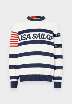 Hvit og marineblå stripet genser med "USA SAILGP"-tekst over brystet, røde striper på venstre erme, og "TOMMY HILFIGER"-tekst på høyre erme.