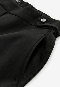 Černé kalhoty s hladkým povrchem, vybavené elastickým pasem a kovovým zapínáním na knoflík. Jednoduchý design a rovný střih.