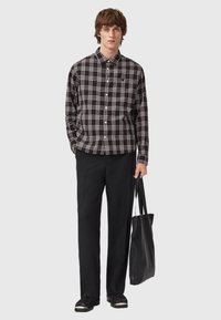 Camicia button-up a quadretti bianco e nero, abbinata a pantaloni neri e una borsa a tracolla nera con texture. Le calzature presentano un sottile accento bianco.