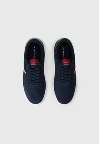 Navy blue sneakers with textured fabric upper, white rubber sole, and red accent stripes. Features black laces and branded tongue label.