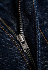 Close-up of silver YKK zipper partially unzipped on dark blue denim fabric with visible orange stitching.