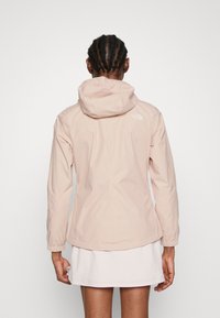 Giacca impermeabile rosa chiaro con cappuccio. Presenta polsini elasticizzati e il logo The North Face sulla parte superiore della schiena. Design minimalista, texture liscia.