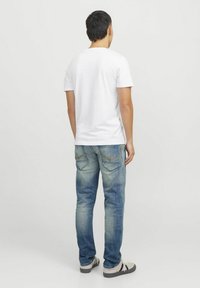 Camiseta blanca de manga corta combinada con jeans de mezclilla azul claro. Los jeans tienen una textura desgastada y costuras visibles en los bolsillos traseros.