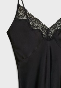 Robe noire sans manches avec fines bretelles et détail floral en dentelle sur l'encolure en V, sur fond clair.