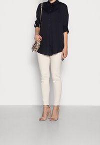 Camicia blu navy con maniche arrotolate, abbinata a jeans skinny color crema e tacchi con cinturini alla caviglia nudi. Borsa a tracolla con stampa serpente.