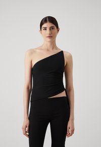 Top nero a spalla unica realizzato in tessuto liscio con dettagli arricciati sul lato. Indossato con pantaloni neri aderenti. Design semplice e moderno.