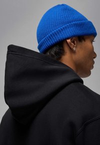 Felpa nera con cappuccio, dal finish testurizzato, con una cucitura del cappuccio ben visibile. Un berretto a coste blu luminoso completa il look.