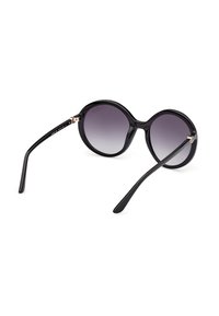 Lunettes de soleil rondes noires avec des verres foncés dégradés et des branches fines et courbées, présentées sur un fond blanc, vues de côté en angle.