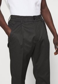 Svarta randiga byxor med skräddarsydd passform, utrustade med knappstängning och sidofickor. Tyget har en slät yta och en formell design.