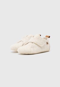 Beige filttofflor med en mjuk textur, med en kardborrebandstängning och en liten brun logotyp på sidan. Rundad tå och lätt sula.