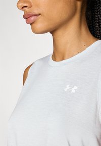 Lyseblå, ermels tanktop til trening med rund hals; har en liten hvit logo på venstre bryst. Glatt tekstur, uformell design.