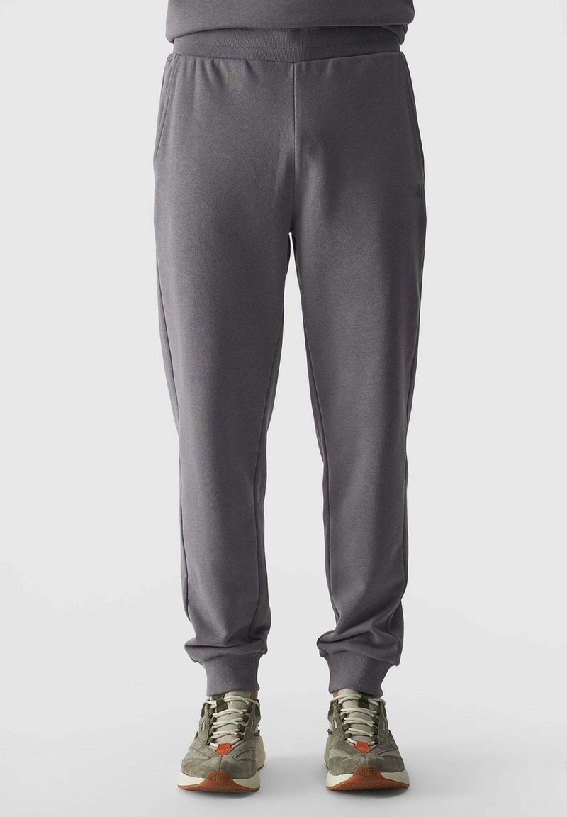 Graue Jogginghosen aus weichem Material, mit elastischem Bund, schmal zulaufenden Beinen und Bündchen an den Knöcheln, kombiniert mit grünen und orangefarbenen Sneakers.
