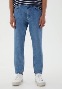 Ljust blå denimjeans med en lös passform, fem fickor och knappstängning. Bärs med vita sneakers.