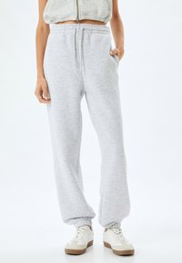 Lichtgrijze sweatpants met een elastische tailleband, zijzakken en geribbelde enkelboorden, gecombineerd met witte en beige sneakers.