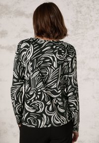 Schwarzes Langarmshirt mit einem weißen abstrakten Muster, aus weichem Stoff gefertigt, mit lockerem Schnitt und rundem Ausschnitt.