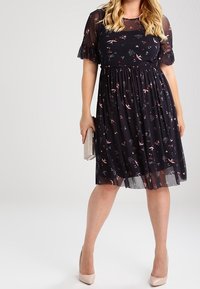 Mörkblå klänning med blommönster och korta, genomskinliga volangärmar. Bodyn har en åtsittande design, medan kjolen är lös och går till knäna.