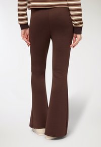 Leggings marroni a zampa realizzati in tessuto elasticizzato, caratterizzati da una texture liscia e un design aderente che si restringe alla caviglia.