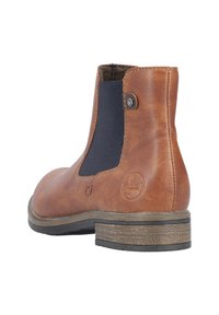 Bottine en cuir brun avec panneaux latéraux élastiques et une semelle en caoutchouc texturée. Elle présente un bout rond et un détail de logo sur le talon.