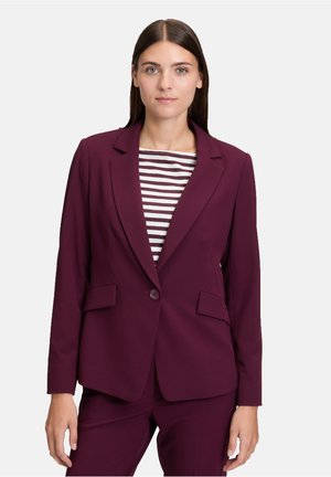 Blazer tagliato bordeaux con risvolti a punta, due tasche frontali e chiusura con singolo bottone. Indossato sopra un top a righe bianco e nere.