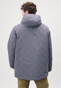 Veste à capuche grise fabriquée dans un matériau lisse et résistant à l'eau. Elle présente une longueur allant jusqu'aux mi-cuisse et une coupe décontractée.