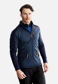Marineblå fleecejakke med sorte ærmer, høj krave og orange lynlåselementer. Har frontlommer og en tætsiddende design.