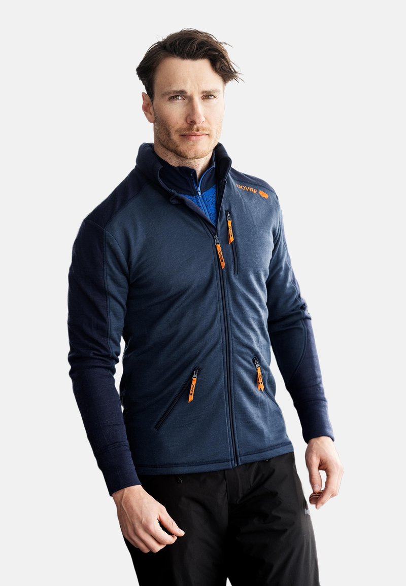 Marineblå fleecejakke med sorte ærmer, høj krave og orange lynlåselementer. Har frontlommer og en tætsiddende design.