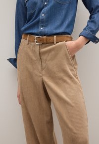 Beige Cordhosen mit vertikalen Streifen, mit lässiger Passform, seitlichen Taschen und einem braunen Ledergürtel auf einem Jeanshemd.