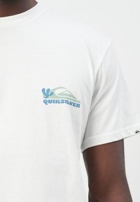 White cotton t-shirt featuring a colorful Quiksilver logo on the left chest, with soft texture and short sleeves.