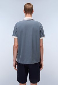 Polo in blu ardesia con finitura testurizzata, dotato di colletto bianco e bordi delle maniche bianchi. Indossato con pantaloni corti blu navy scuri.