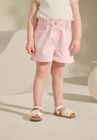 Shorts rayés roses avec une taille élastique, associés à des sandales à lanières blanches. Le tissu semble léger et doux.