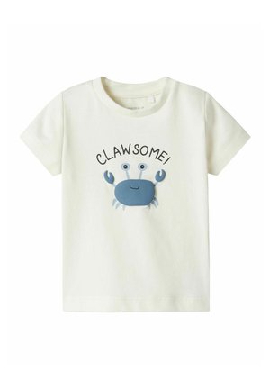 T-shirt in cotone color crema chiaro con grafica di un granchio blu e la parola "CLAW-SOME!" stampata sopra in nero. Design con maniche corte e colletto a girocollo.