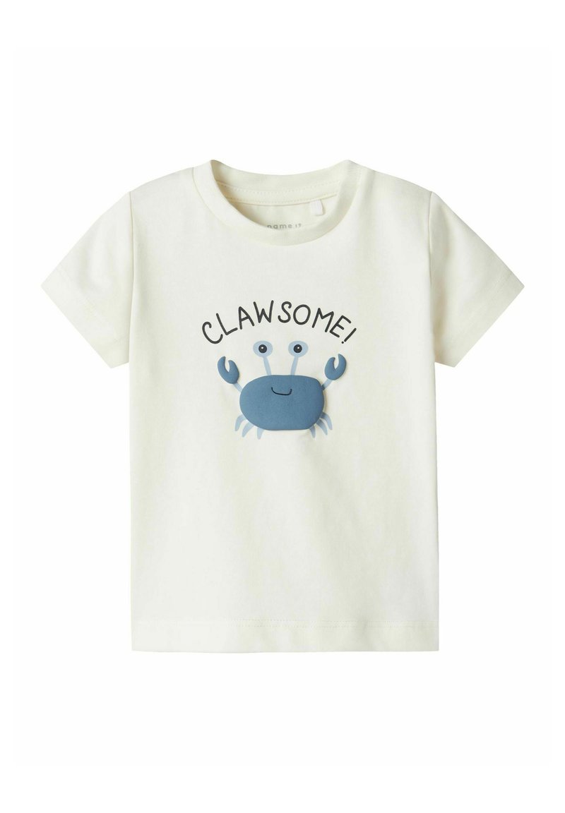 T-shirt in cotone color crema chiaro con grafica di un granchio blu e la parola "CLAW-SOME!" stampata sopra in nero. Design con maniche corte e colletto a girocollo.